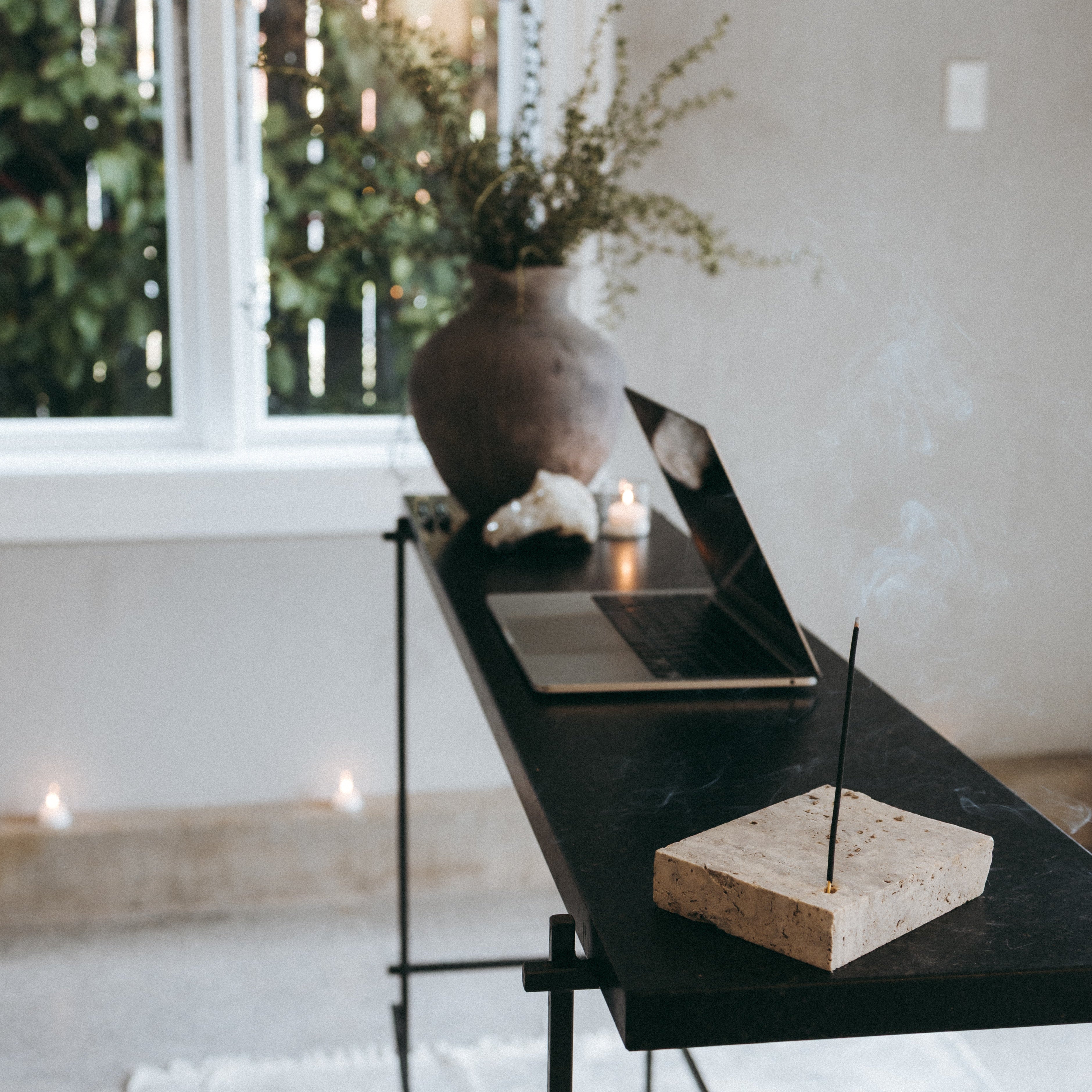 Black marble table with a vase, candles, and a plant in a room with a window and light-colored walls.