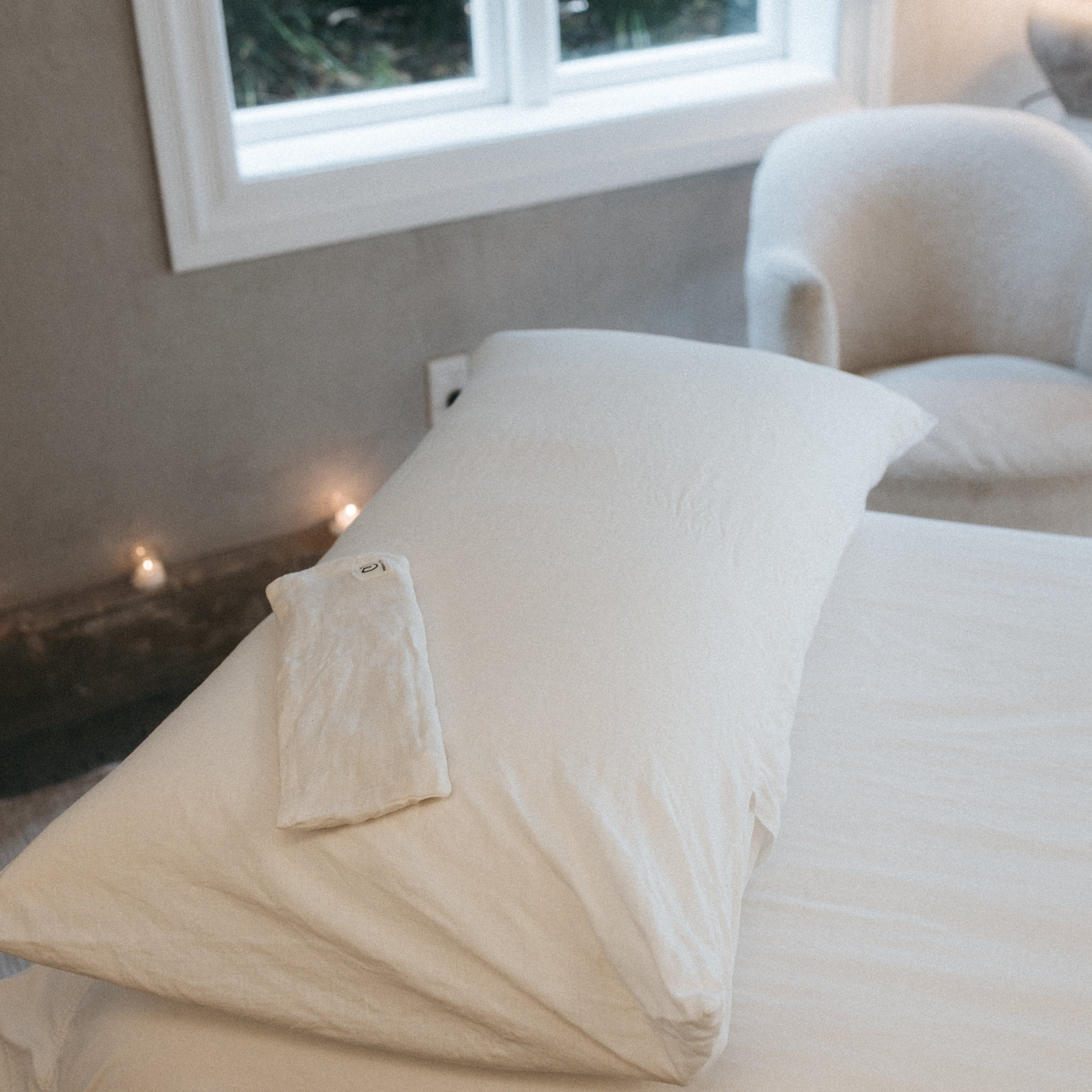 Neatly made bed with white bedding in a room with a window and chair.